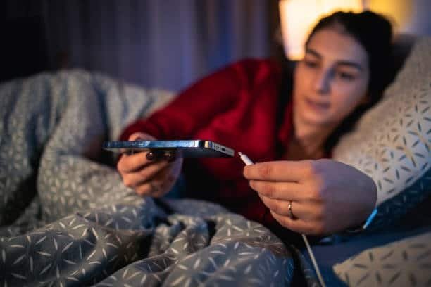 Woman using USB Type-C cable to charge smartphone in bed.