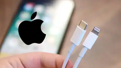 hand holding Apple Lightning cable and USB-C cable with Apple logo in background