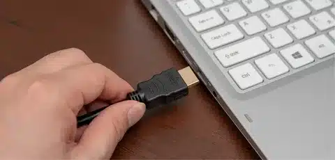 hand inserting connector cable into laptop charging port